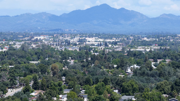 Aerial view of the city of Redding surrounded by lush green trees and rolling hills with distant mountains under a clear sky in Redding California United States. Aerial view of the city of Redding surrounded by lush green trees and rolling hills with distant mountains under a clear sky in Redding California United States.