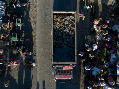 Aerial view of a truck carrying stones through a busy roadside market with people and stalls in Kemalang Central Java Indonesia.
