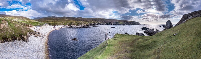 Aerial view of the rugged coastline and pebble beach at An Port with green grassy cliffs and the Atlantic Ocean under a dramatic cloudy sky in Ardara County Donegal Ireland.