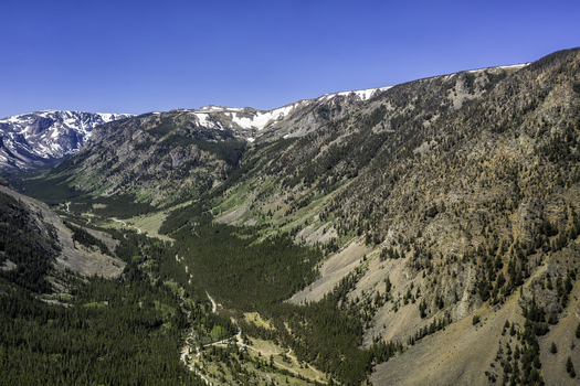Aerial view of Beartooth Pass showing rugged mountain slopes evergreen forests and snow capped peaks under a clear blue sky in Park County Wyoming United States. Aerial view of Beartooth Pass showing rugged mountain slopes evergreen forests and snow capped peaks under a clear blue sky in Park County Wyoming United States.