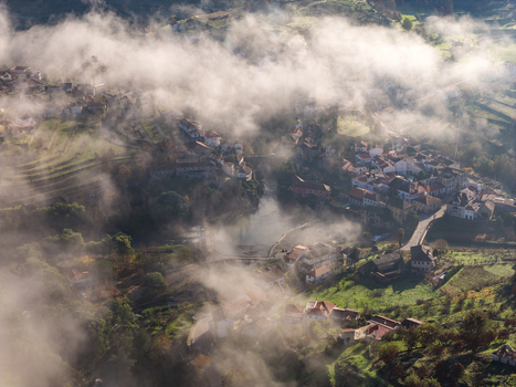 Aerial view of the historic village of Avo shrouded in morning mist and fog with red tiled houses and green terraced hills Oliveira do Hospital Coimbra District Portugal.