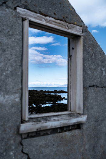 View of an abandoned farmhouse window framing the rocky coastline and blue sea under a cloudy sky Hafnarfjordur Hafnarfjardarkaupstad Iceland. View of an abandoned farmhouse window framing the rocky coastline and blue sea under a cloudy sky Hafnarfjordur Hafnarfjardarkaupstad Iceland.