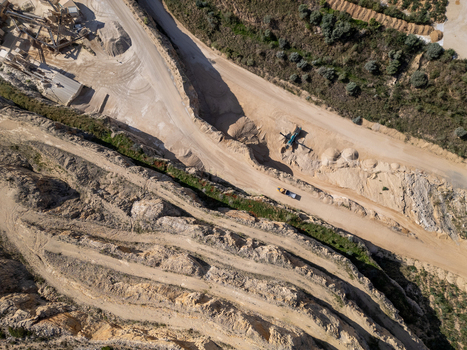 Aerial view of an active stone quarry with terraced rock faces heavy machinery and dirt access roads in Teulada Valencian Community Spain.