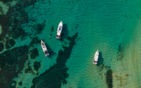 Aerial view of three boats floating in the clear turquoise waters over a coral reef in Kecamatan Denpasar Selatan Bali Indonesia.