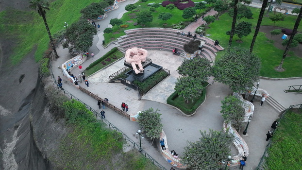 Aerial view of the iconic El Beso sculpture in Parque del Amor surrounded by lush gardens mosaic walls and walking paths along the cliffside in Miraflores Provincia de Lima Peru.