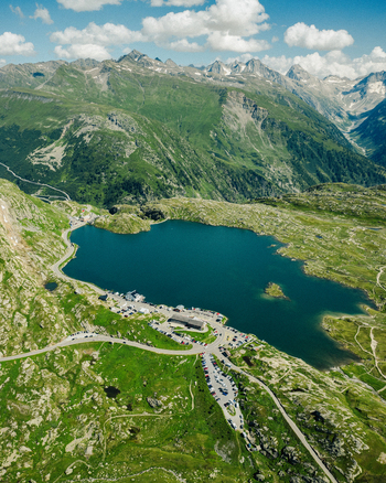 Aerial view of Totensee lake at Grimsel Pass with winding mountain roads and parked cars surrounded by alpine peaks in Obergoms Valais Switzerland.