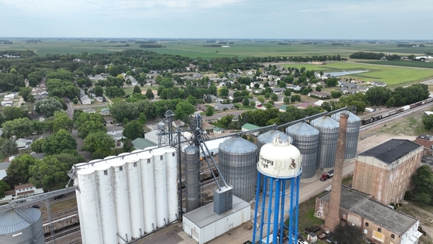 Aerial view of grain elevators and a water tower rise amidst a landscape of green fields and clustered houses Waseca Minnesota United States.