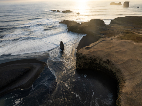 Aerial view of Dyrholaey promontory with dramatic black sand beach crashing waves and rocky sea stacks illuminated by golden hour light in Myrdalshreppur Iceland. Aerial view of Dyrholaey promontory with dramatic black sand beach crashing waves and rocky sea stacks illuminated by golden hour light in Myrdalshreppur Iceland.