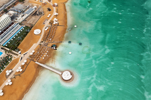 Aerial view of a vibrant Dead Sea resort golden sands and white parasols meet the striking turquoise waters Ein Bokek Israel. Aerial view of a vibrant Dead Sea resort golden sands and white parasols meet the striking turquoise waters Ein Bokek Israel.