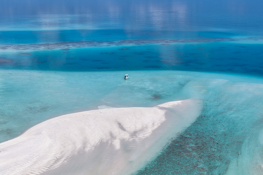 Aerial view of lush tropical islands with green palm trees and turquoise coral reefs surrounded by the deep blue ocean under a clear sky near Vaanee Dhaalu Atoll Maldives. Aerial view of lush tropical islands with green palm trees and turquoise coral reefs surrounded by the deep blue ocean under a clear sky near Vaanee Dhaalu Atoll Maldives.