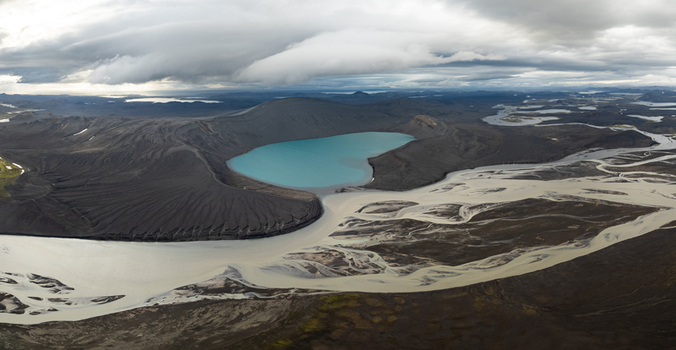 Aerial view of Landmannalaugar featuring a vibrant turquoise lake nestled within dark volcanic terrain and braided glacial rivers under a dramatic cloudy sky in Rangarthing ytra Iceland. Aerial view of Landmannalaugar featuring a vibrant turquoise lake nestled within dark volcanic terrain and braided glacial rivers under a dramatic cloudy sky in Rangarthing ytra Iceland.