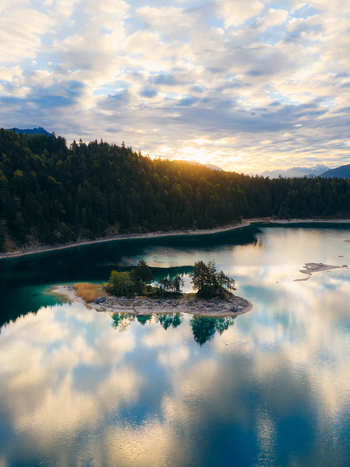 Aerial view of Eibsee lake with a small wooded island surrounded by dense evergreen forests and reflecting clouds during a golden sunset Grainau Bavaria Germany. Aerial view of Eibsee lake with a small wooded island surrounded by dense evergreen forests and reflecting clouds during a golden sunset Grainau Bavaria Germany.