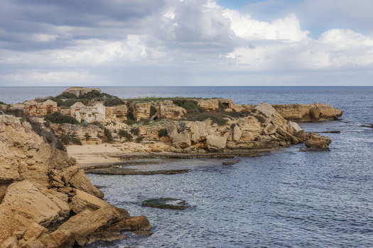 View of the rocky coastline with ancient stone ruins overlooking the Mediterranean Sea under a cloudy sky Syracuse Sicily Italy.