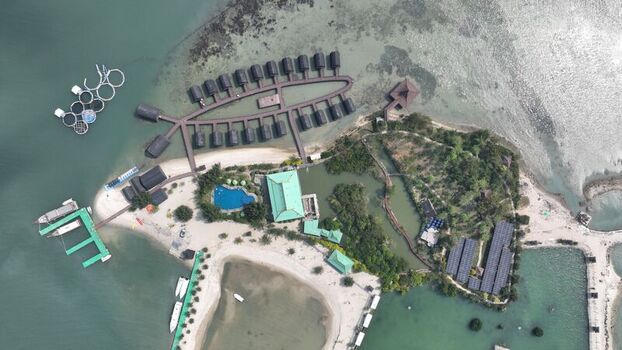 Aerial view of Pulau Lima Resort featuring overwater bungalows arranged in a fish shape a swimming pool and a sandy beach surrounded by clear turquoise waters in Kasemen Banten Indonesia. Aerial view of Pulau Lima Resort featuring overwater bungalows arranged in a fish shape a swimming pool and a sandy beach surrounded by clear turquoise waters in Kasemen Banten Indonesia.