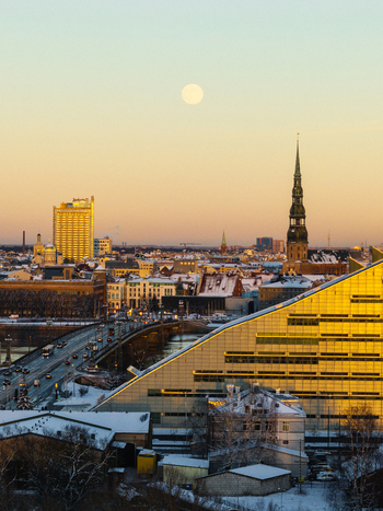 Aerial view of the National Library of Latvia and St. Peters Church illuminated by sunset light with a full moon over the snow covered city of Riga Latvia. Aerial view of the National Library of Latvia and St. Peters Church illuminated by sunset light with a full moon over the snow covered city of Riga Latvia.