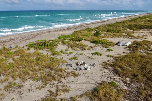 Aerial view of turquoise waves crashing onto the sandy shore a contrast to the grassy dunes and weathered structures nestled along the coast Jupiter Island Florida United States. Aerial view of turquoise waves crashing onto the sandy shore a contrast to the grassy dunes and weathered structures nestled along the coast Jupiter Island Florida United States.