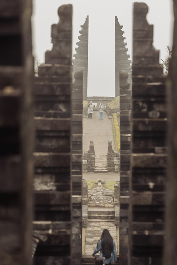 View of the historic Cetho Temple with its iconic split stone gateways and people walking along the path under a misty sky in Kecamatan Jenawi Jawa Tengah Indonesia. View of the historic Cetho Temple with its iconic split stone gateways and people walking along the path under a misty sky in Kecamatan Jenawi Jawa Tengah Indonesia.