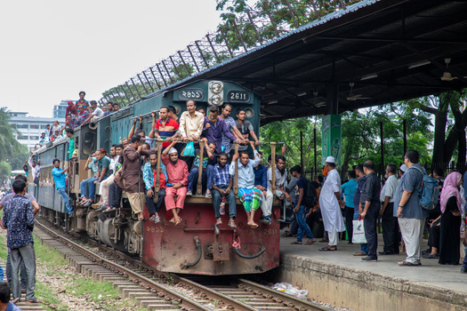Dhaka Bangladesh 14 June 2018 View of Airport Railway Station with a crowded train arriving as passengers hang from the locomotive and stand on the platform under a covered roof. Dhaka Bangladesh 14 June 2018 View of Airport Railway Station with a crowded train arriving as passengers hang from the locomotive and stand on the platform under a covered roof.