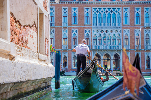 Venice Italy 29 March 2026 View of a gondolier navigating the vibrant green waters of a canal framed by weathered walls and the ornate facade of a building. Venice Italy 29 March 2026 View of a gondolier navigating the vibrant green waters of a canal framed by weathered walls and the ornate facade of a building.