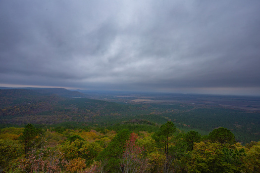 View of vast green forests and distant hills under a moody expansive sky with a tapestry of autumn colors painting the landscape Arkansas United States. View of vast green forests and distant hills under a moody expansive sky with a tapestry of autumn colors painting the landscape Arkansas United States.