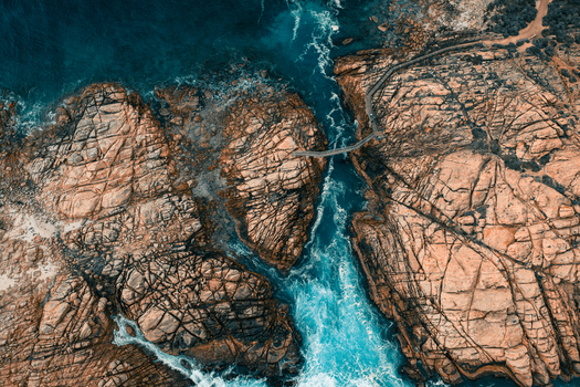 Aerial view of Canal Rocks Bridge spanning rugged rock formations with turquoise ocean water and crashing waves in Yallingup Western Australia Australia.