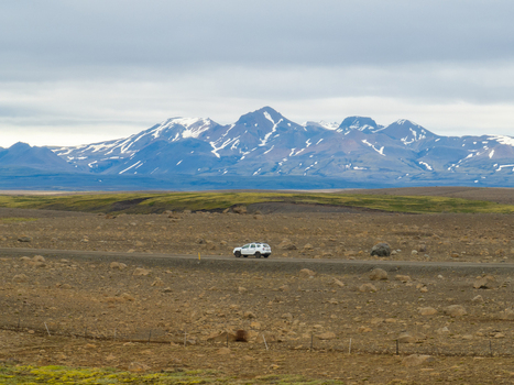 Aerial view of a white SUV driving on a gravel road through the volcanic landscape of Kerlingarfjoll with snow capped mountains in the background in Hrunamannahreppur Iceland. Aerial view of a white SUV driving on a gravel road through the volcanic landscape of Kerlingarfjoll with snow capped mountains in the background in Hrunamannahreppur Iceland.