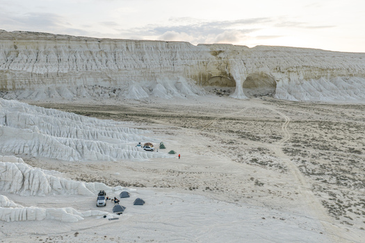 Aerial view of Tuzbair salt flats with camping tents and off road vehicles parked near white limestone cliffs in Mangystau District Mangystau Region Kazakhstan.