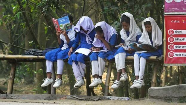 View of schoolgirls reading books on a bamboo bench Bangladesh.