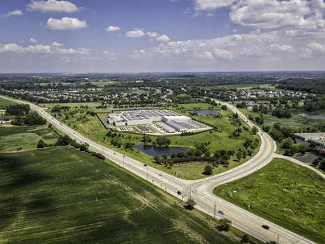 Aerial view of an industrial facility with solar panels on the roof surrounded by lush green fields small ponds and intersecting roads in Volo Illinois United States. Aerial view of an industrial facility with solar panels on the roof surrounded by lush green fields small ponds and intersecting roads in Volo Illinois United States.