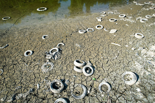 Aerial view of discarded tires scattered across a cracked and parched riverbed under bright sunlight in Carignano Piemonte Italy. Aerial view of discarded tires scattered across a cracked and parched riverbed under bright sunlight in Carignano Piemonte Italy.