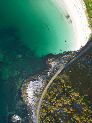 Aerial view of Vik Strand featuring turquoise water white sand and a coastal road winding through rocky terrain and autumn foliage in Leknes Nordland Norway. Aerial view of Vik Strand featuring turquoise water white sand and a coastal road winding through rocky terrain and autumn foliage in Leknes Nordland Norway.