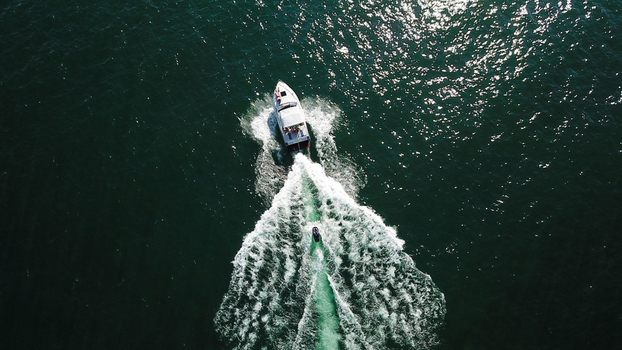 Aerial view of a white motorboat and a jet ski cruising through dark green water with white foam wakes Saint Prex Vaud Switzerland.