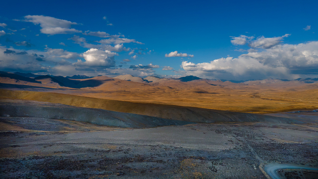 Aerial view of the vast Deosai Plains with rolling golden hills rugged terrain and dramatic cloud formations under a clear blue sky in Skardu Gilgit Pakistan. Aerial view of the vast Deosai Plains with rolling golden hills rugged terrain and dramatic cloud formations under a clear blue sky in Skardu Gilgit Pakistan.