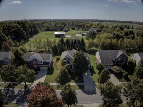 Aerial view of suburban houses with driveways lush green lawns and mature trees with a large open field and a barn in the background in Mason Ohio United States.