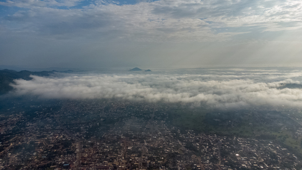 Aerial view of the city of Ho partially covered by a thick layer of morning mist with distant mountains under a cloudy sky in Ho Volta Region Ghana. Aerial view of the city of Ho partially covered by a thick layer of morning mist with distant mountains under a cloudy sky in Ho Volta Region Ghana.