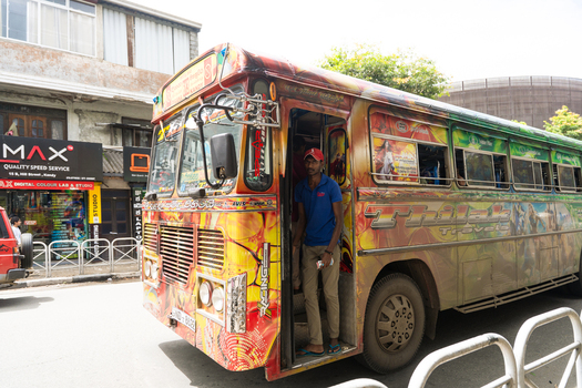 Sri Lanka 20 February 2026 View of a colorful decorated bus in Kandy parked on a city street with a man standing in the open doorway and shops in the background.