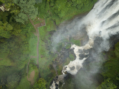 Aerial view of water plunging down into a misty abyss besides lush green vegetation Curugsewu Kendal Regency Central Java Indonesia. Aerial view of water plunging down into a misty abyss besides lush green vegetation Curugsewu Kendal Regency Central Java Indonesia.