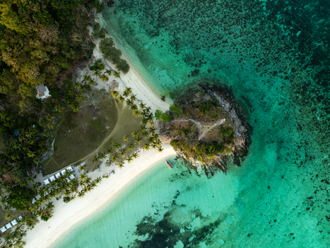 Aerial view of Malcapuya Island with its white sand beach turquoise waters lush palm trees and a small boat anchored off the coast in Coron Mimaropa Philippines. Aerial view of Malcapuya Island with its white sand beach turquoise waters lush palm trees and a small boat anchored off the coast in Coron Mimaropa Philippines.
