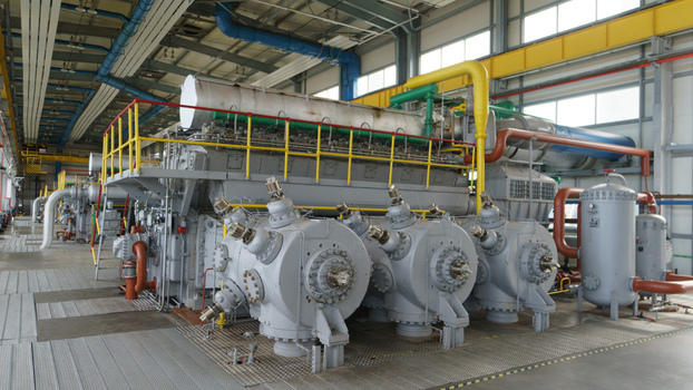 View of a large industrial gas compressor engine inside a power plant facility with complex piping systems yellow safety railings and metal flooring in Latvia. View of a large industrial gas compressor engine inside a power plant facility with complex piping systems yellow safety railings and metal flooring in Latvia.