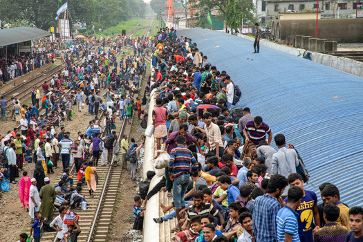 Dhaka Bangladesh 14 June 2018 View of Airport Railway Station crowded with people sitting on the roof of a train and standing along the tracks during a busy commute. Dhaka Bangladesh 14 June 2018 View of Airport Railway Station crowded with people sitting on the roof of a train and standing along the tracks during a busy commute.