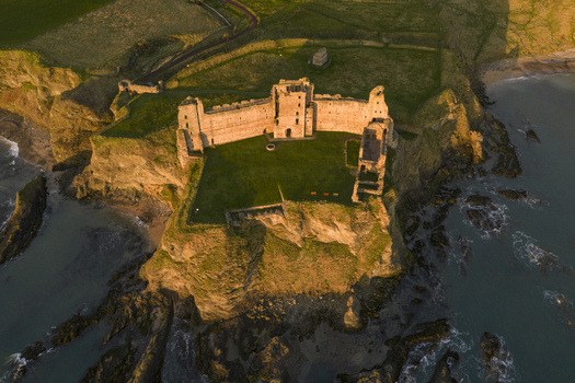 Aerial view of Tantallon Castle ruins perched on a steep cliff overlooking the North Sea during golden hour in North Berwick Scotland United Kingdom.