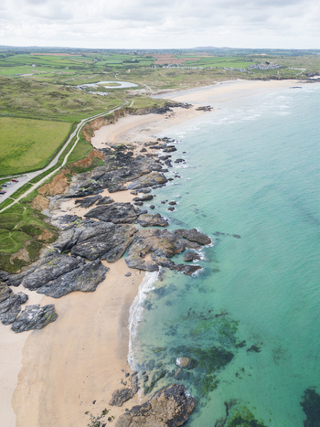 Aerial view of Godrevy Beach with dark jagged rocks turquoise sea water sandy shores and green coastal cliffs in Gwithian England United Kingdom. Aerial view of Godrevy Beach with dark jagged rocks turquoise sea water sandy shores and green coastal cliffs in Gwithian England United Kingdom.