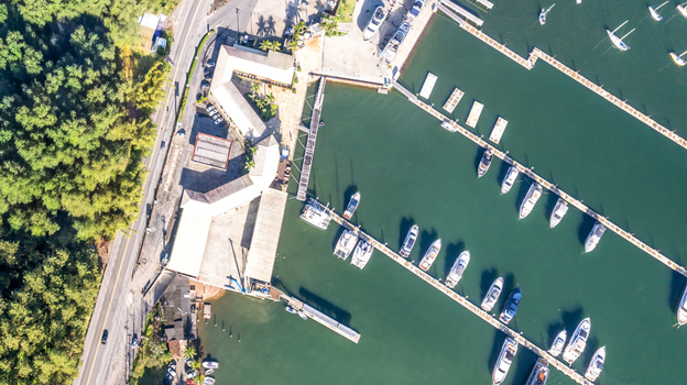 Aerial view of a marina with numerous boats docked at wooden piers surrounded by lush green forest and a coastal road in Angra dos Reis Rio de Janeiro Brazil.