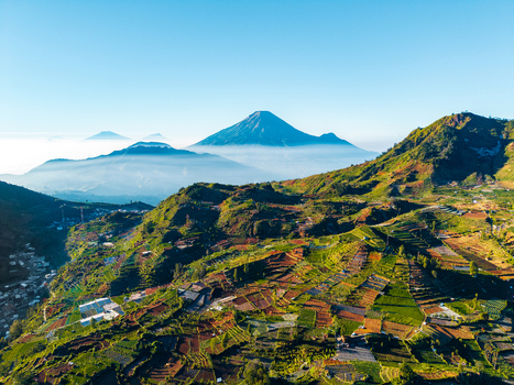 Aerial view of Mount Sindoro with terraced fields and volcanic peaks under a clear sky in Kecamatan Kejajar Jawa Tengah Indonesia. Aerial view of Mount Sindoro with terraced fields and volcanic peaks under a clear sky in Kecamatan Kejajar Jawa Tengah Indonesia.