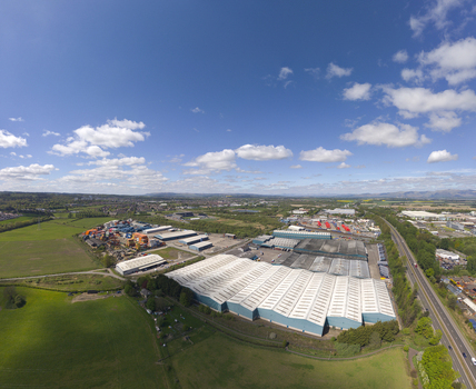 Aerial view of large industrial warehouses and commercial buildings surrounded by green fields under a blue sky with clouds in Grangemouth Scotland United Kingdom.