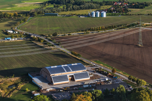 Aerial view of a modern industrial building with solar panels on the roof surrounded by agricultural fields power lines and rural landscape in Uckermark Brandenburg Germany. Aerial view of a modern industrial building with solar panels on the roof surrounded by agricultural fields power lines and rural landscape in Uckermark Brandenburg Germany.