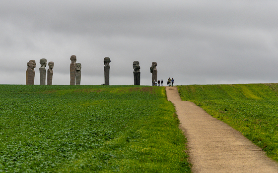 View of the Dodekalitten stone sculptures standing in a green field with a walking path and people under a cloudy sky in Kragenaes Lolland Denmark. View of the Dodekalitten stone sculptures standing in a green field with a walking path and people under a cloudy sky in Kragenaes Lolland Denmark.