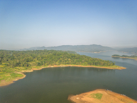 Aerial view of the Karanganyar reservoir area featuring lush green hills calm water and agricultural fields under a clear blue sky in Wadaslintang Central Java Indonesia. Aerial view of the Karanganyar reservoir area featuring lush green hills calm water and agricultural fields under a clear blue sky in Wadaslintang Central Java Indonesia.