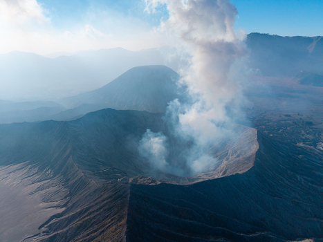 Aerial view of Mount Bromo volcano crater emitting smoke with rugged volcanic landscape and hazy sky in Tosari East Java Indonesia.
