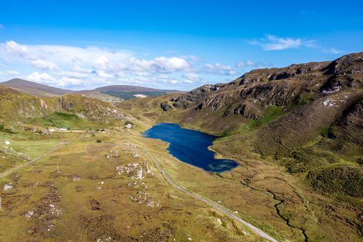 Aerial view of An Port lake surrounded by rugged mountains green hills and rocky terrain with a winding road in the valley in Ardara County Donegal Ireland.